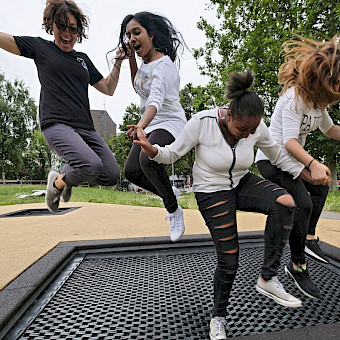 Mädchen springen mit einer Sozialarbeiterin auf einem Trampolin.