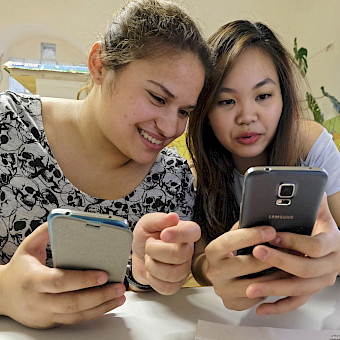 Mädchen schauen in ihre Smartphones und tauschen sich über Nachrichten aus.